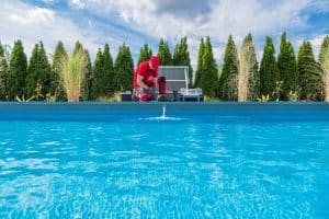 Pool technician inspecting or repairing a swimming pool with tools nearby.
